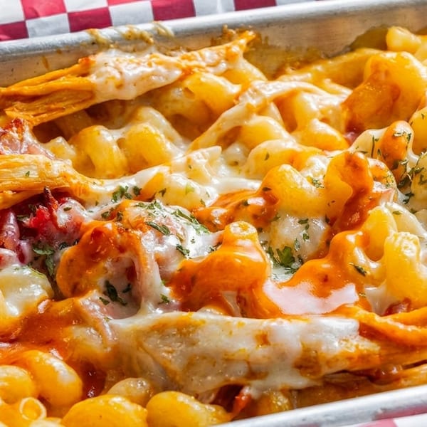 Close-up of baked macaroni and cheese with chicken, bacon, and melted cheese in a metal pan.
