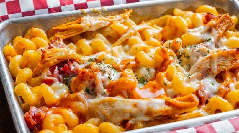 Baked macaroni and cheese with chicken, bacon, and melted cheese in a metal tray.