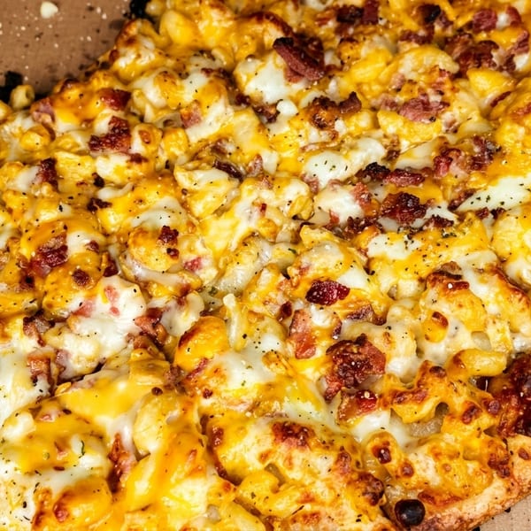 Close-up of a mac and cheese pizza with bacon bits in a cardboard box.