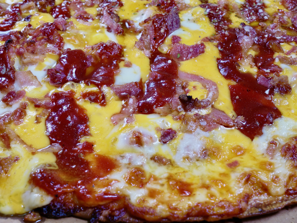 A close up of The Gunslinger pizza that has a garlic butter BBQ base, chicken, 2x bacon, and cheddar cheese.