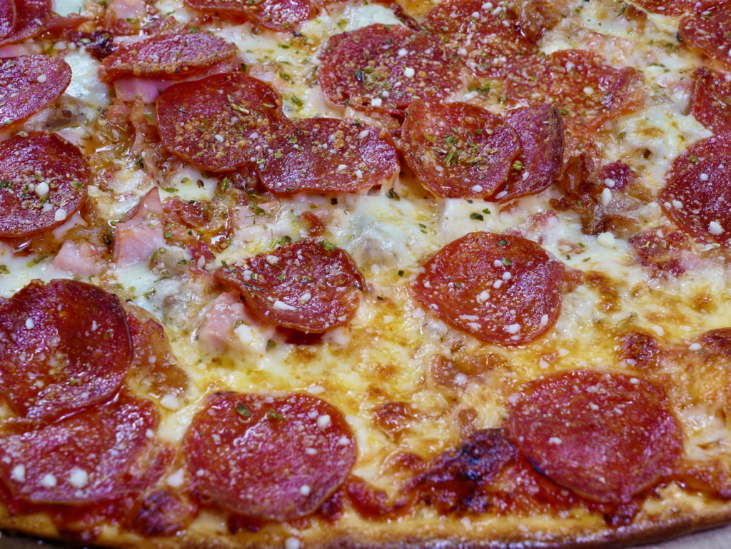 A close up of The Homer pizza that has sausage, pepperoni, ham, bacon, and garlic.