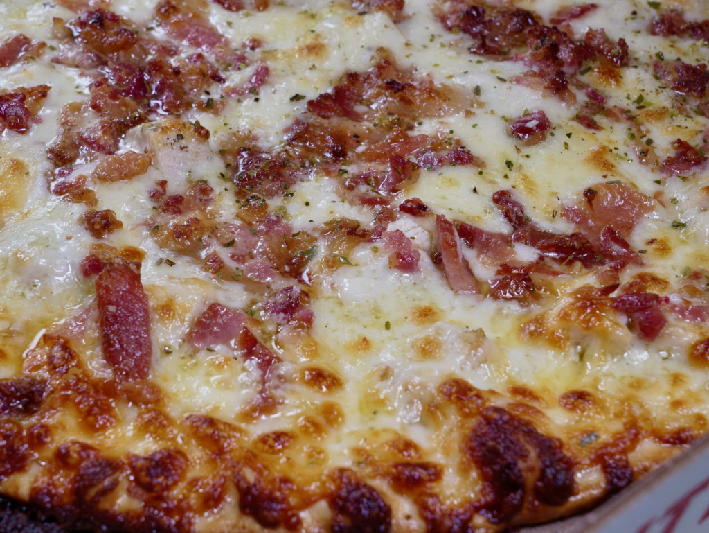 A close up of The Karate pizza that has a garlic butter ranch base, ranch chicken, pepperoni, and bacon.