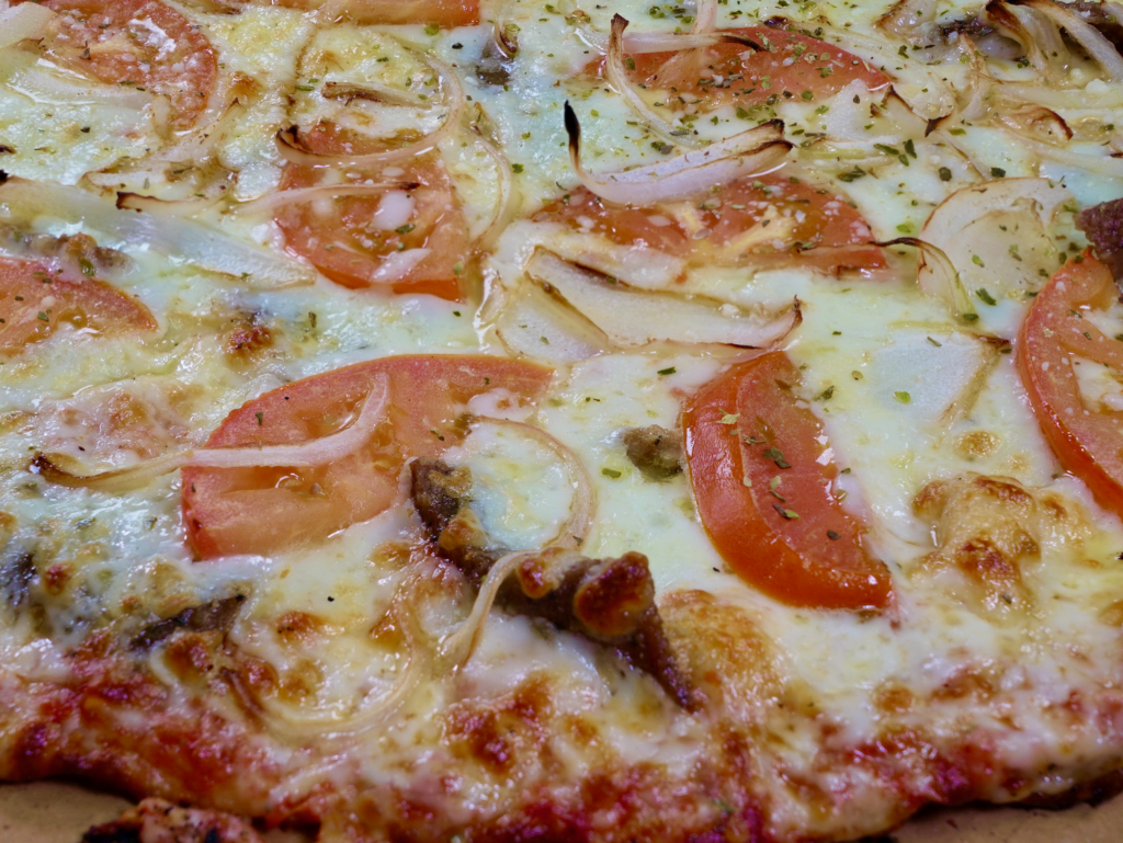 A close up of The Odyssey pizza that is a tomato base pizza with gyro meat, tomato, onion, and a side of tzatziki sauce.