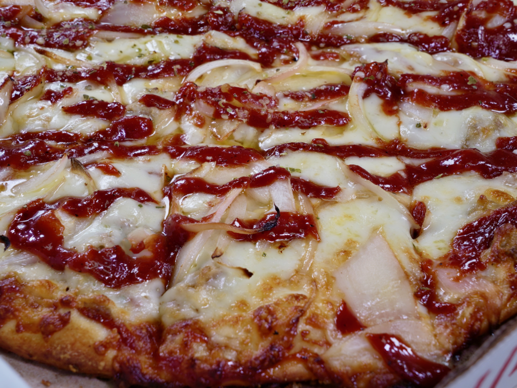A close up of The Smokehouse pizza that has a garlic butter base, pulled pork, BBQ sauce, and onions.